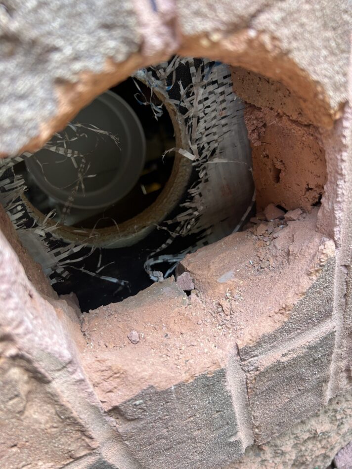 Photo of hole drilled at front wall of home through brick with radon discharge pipe from interior visible.