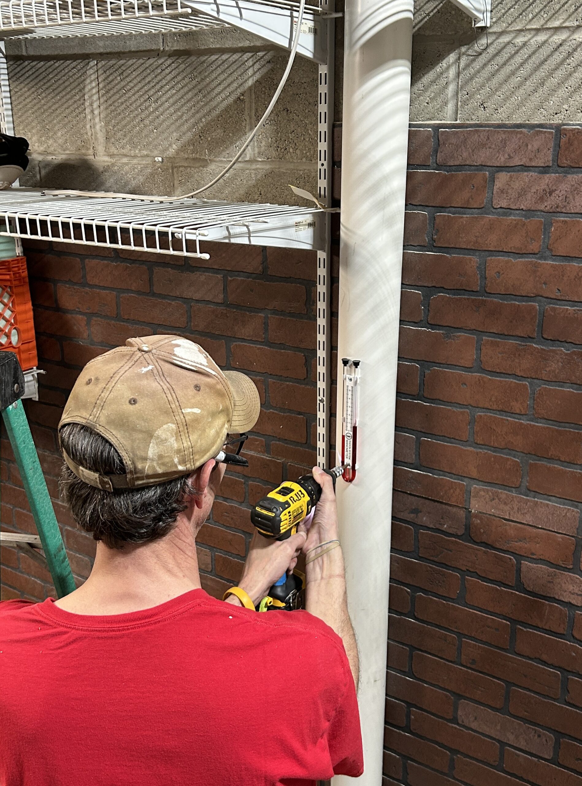 Photo of a contractor installing a manometer on a white pipe in a basement.