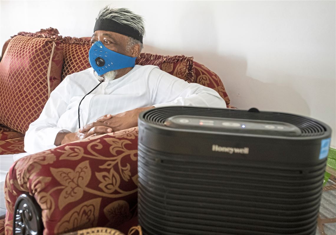 an older man sits on a couch next to a Honeywell Portable Air Cleaner