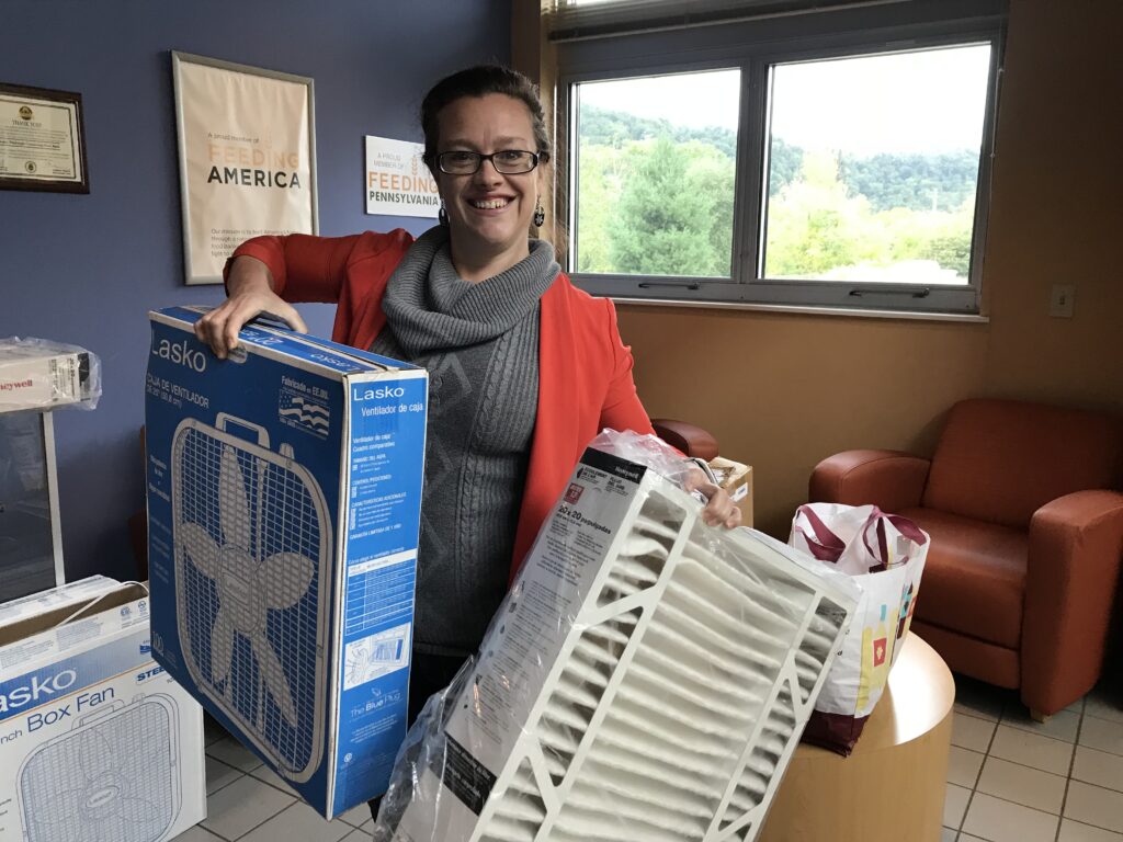 A woman holding a box fan and filter to make a DIY fan filter