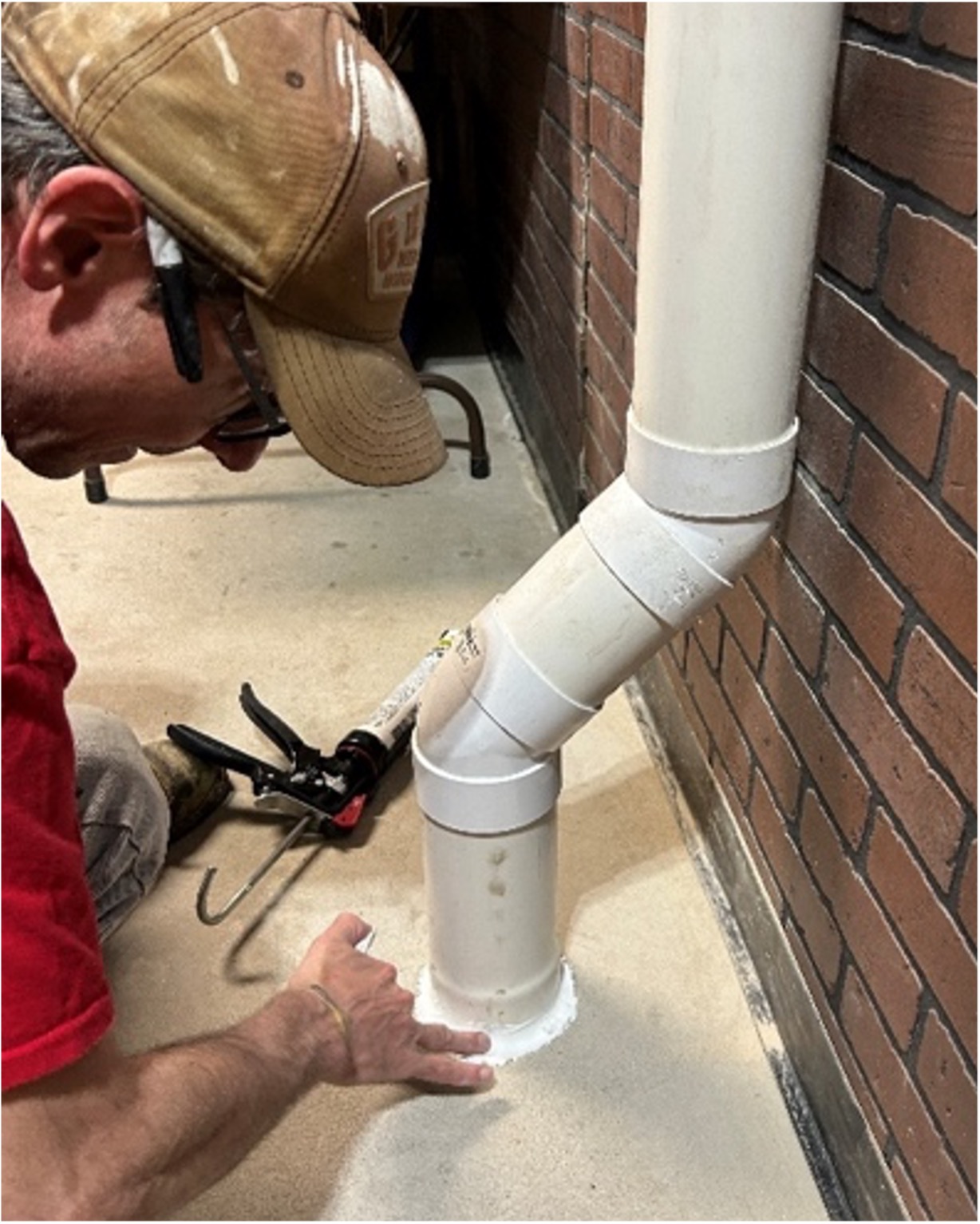 Photo showing a contractor caulking around a pipe emerging from a basement floor.
