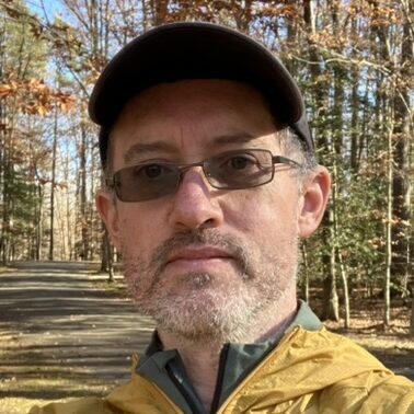 Photo of Bill Collinge in a baseball cap, glasses, and a yellow jacket