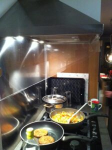 Photograph of a kitchen stove with food cooking. Two plexiglass flanges are attached to the side of the range hood to help direct airflow from the cooking surfaces towards the fan.