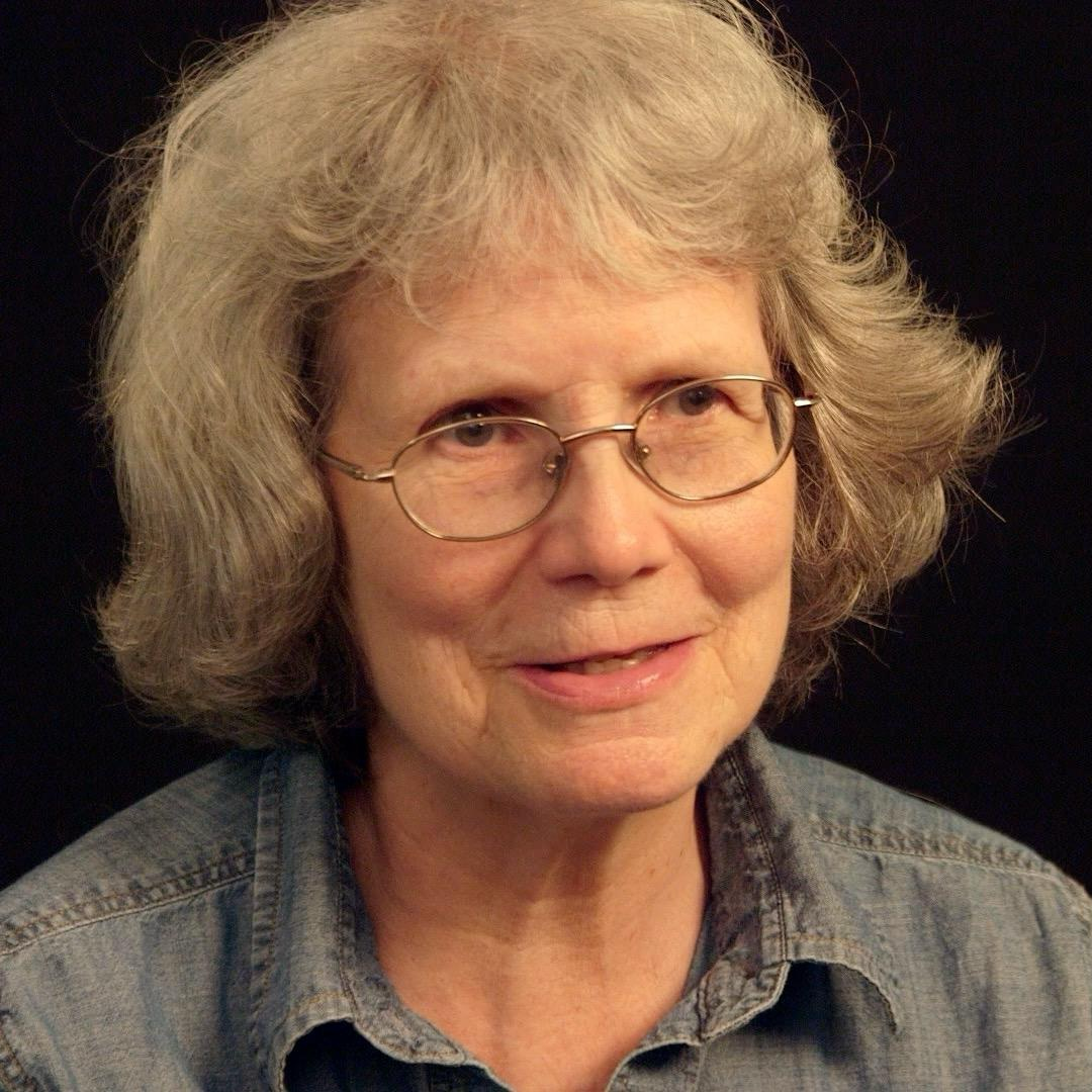 Photo of Linda Wigington wearing a blue shirt and glasses. She appears to be speaking to the camera.