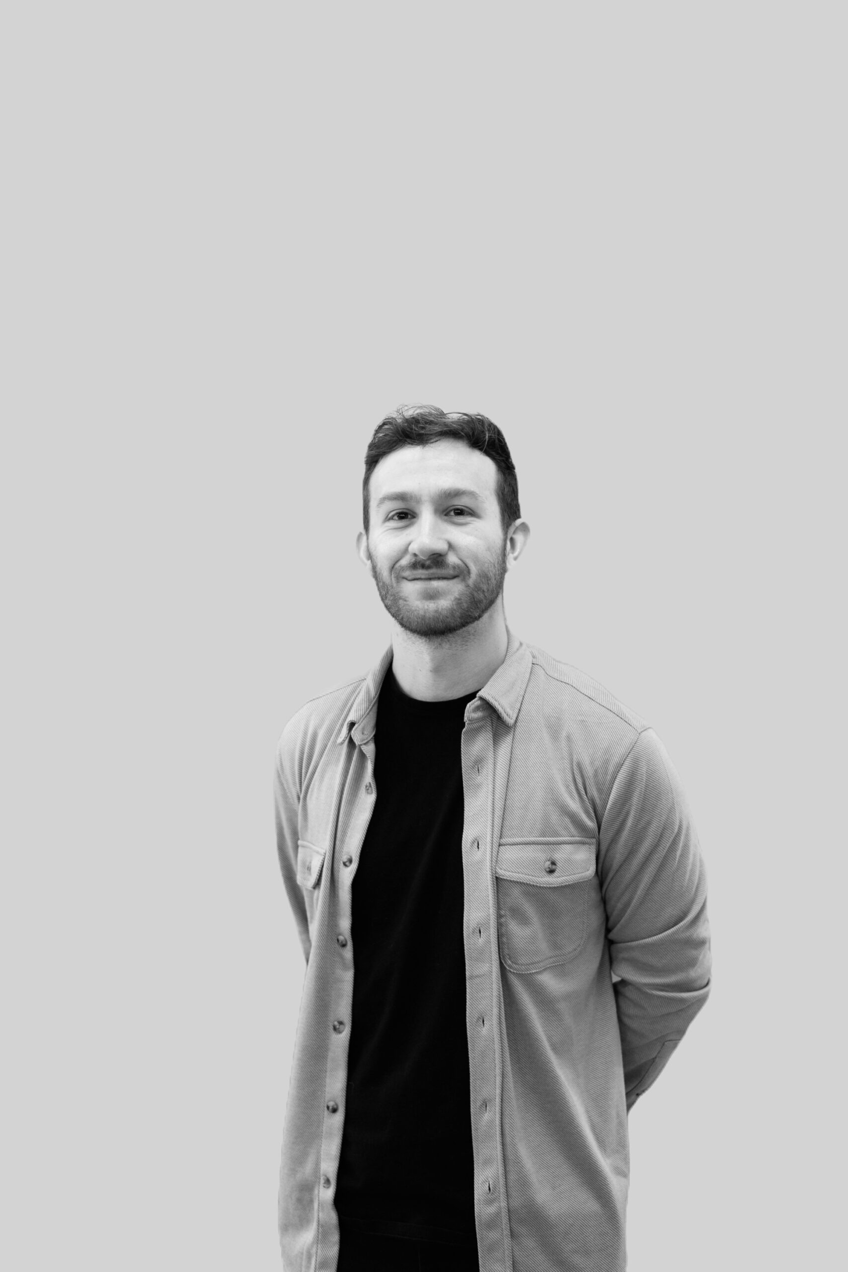 Black and white photo of Matt Oriente, a bearded man with his hands clasped behind his back