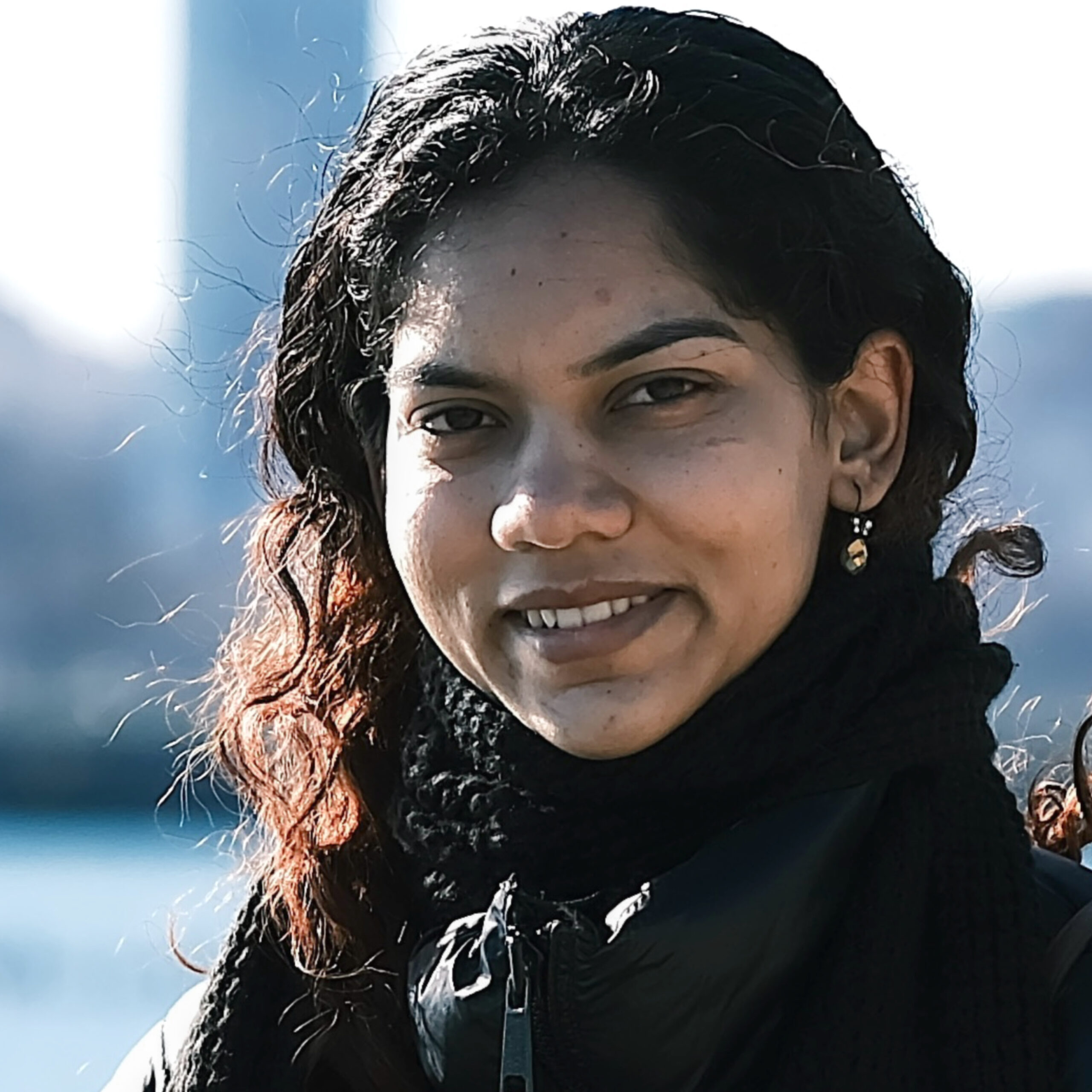 Photo of Naveena Nagaraju wearing a dark coat and standing in front of a blurred skyline