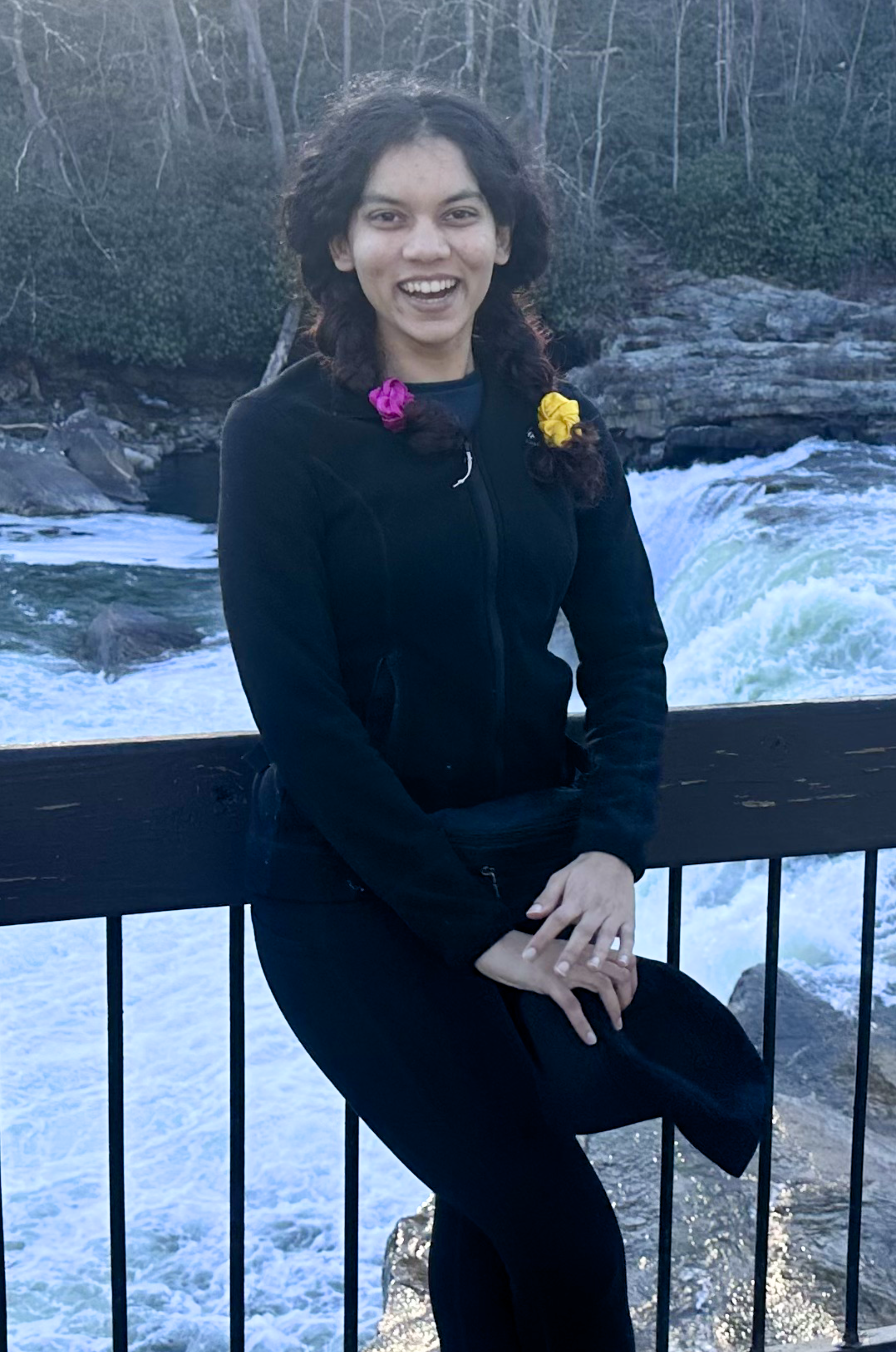 Photo of Naveena leaning against a railing in front of a flowing river