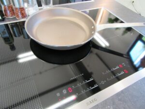 Photograph of an induction stovetop with a metal frying pan on it.
