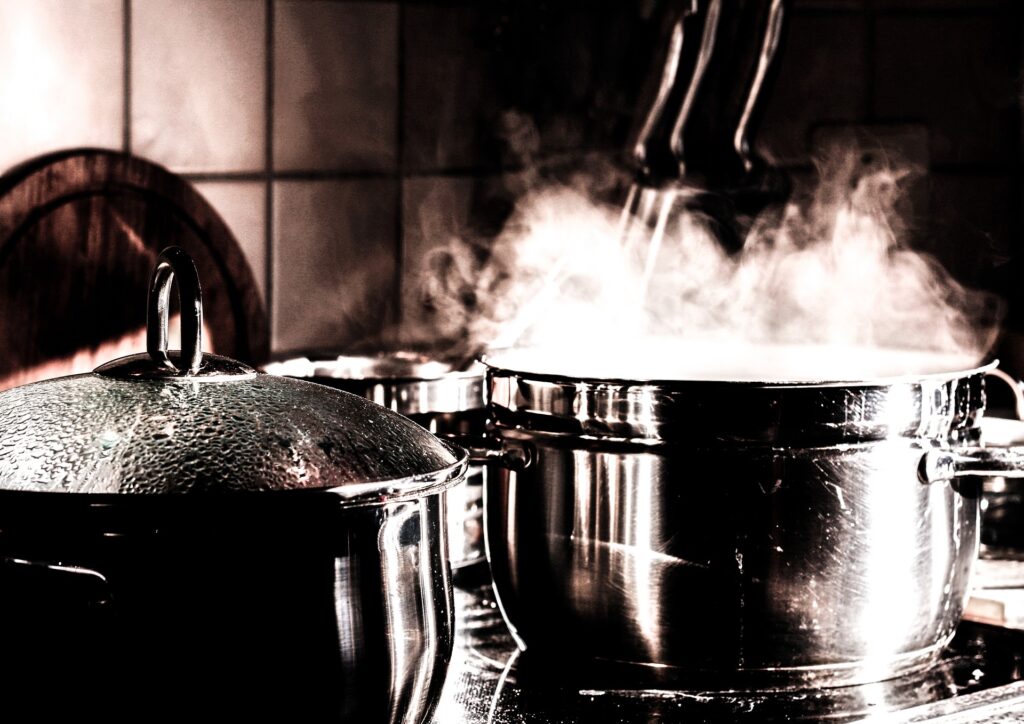 Two pots on a stovetop, one with a lid on, one steaming into the kitchen.