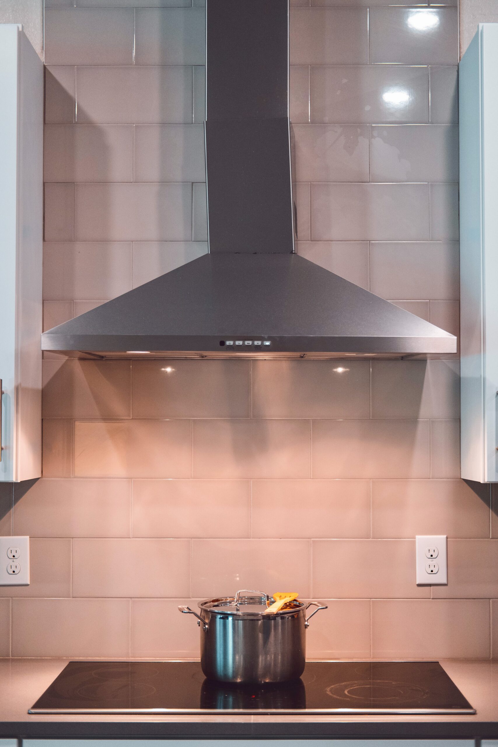 Photo of a kitchen stovetop with a pot on it and a range hood above it.